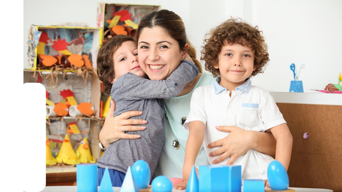 A smiling childcare provider with two children in a colorful classroom